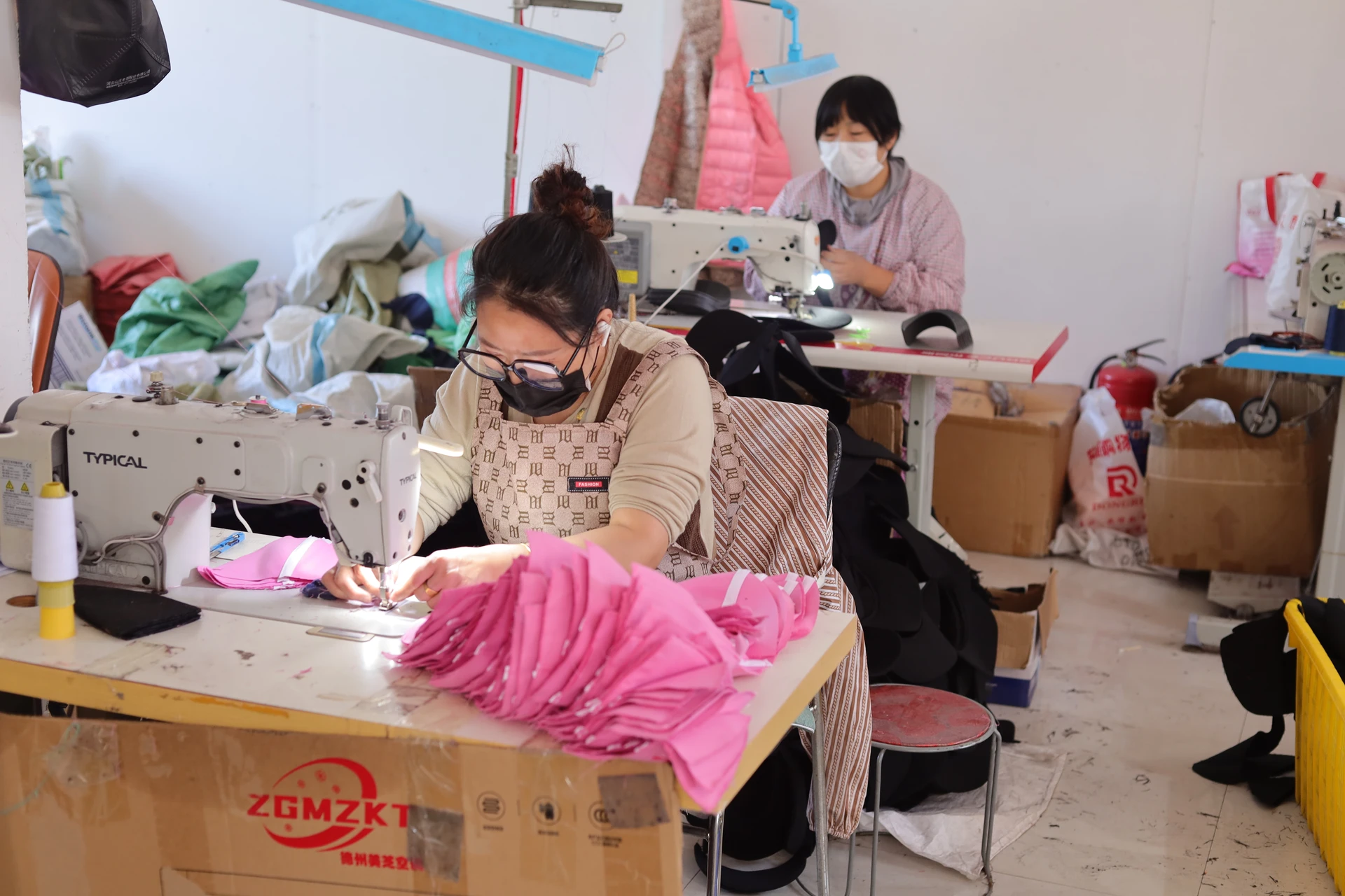 Two cap sewing operators working with pink cut fabric panels in a real workshop
