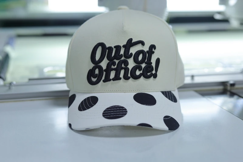Cream cap with raised black front lettering and black polka dots on a light curved visor