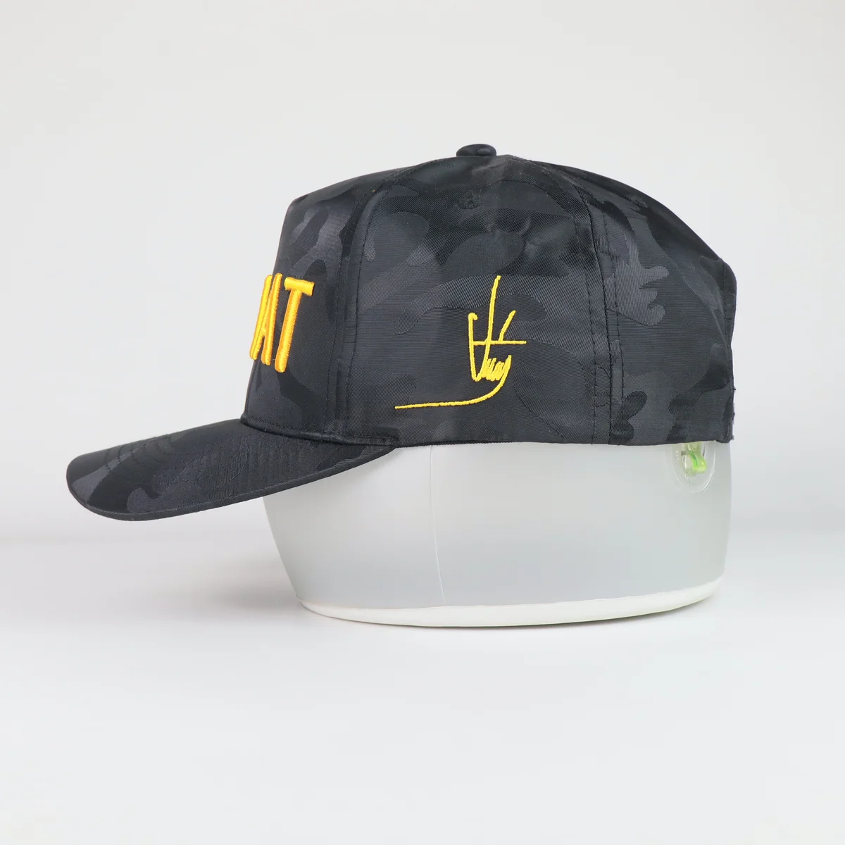 Side profile of dark camouflage cap showing yellow side logo embroidery