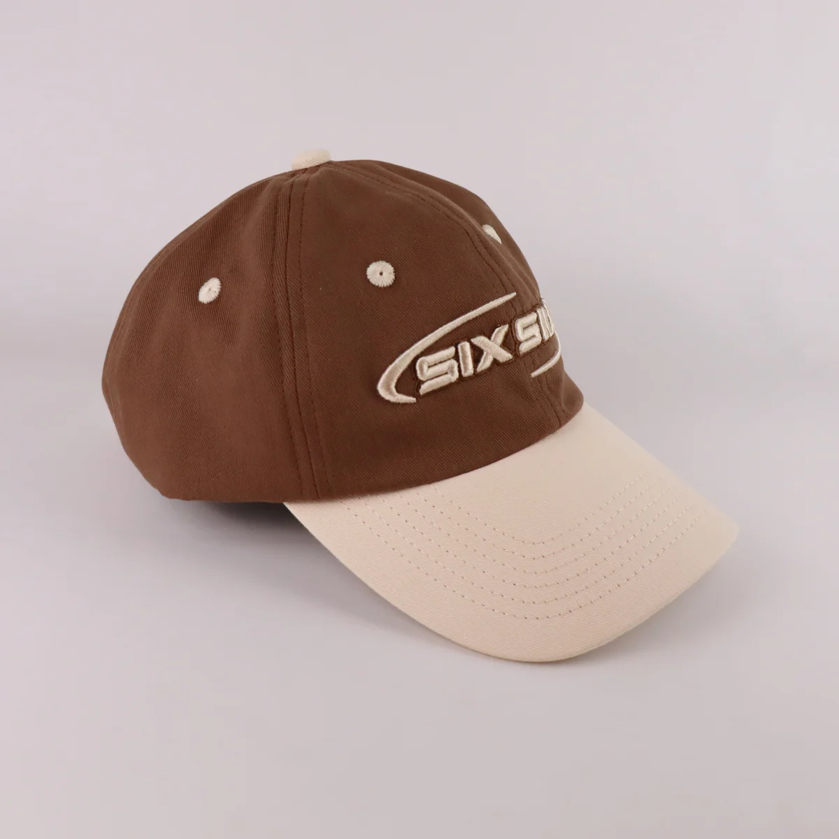 Angled front of a brown and cream curved-brim cap with raised embroidered lettering