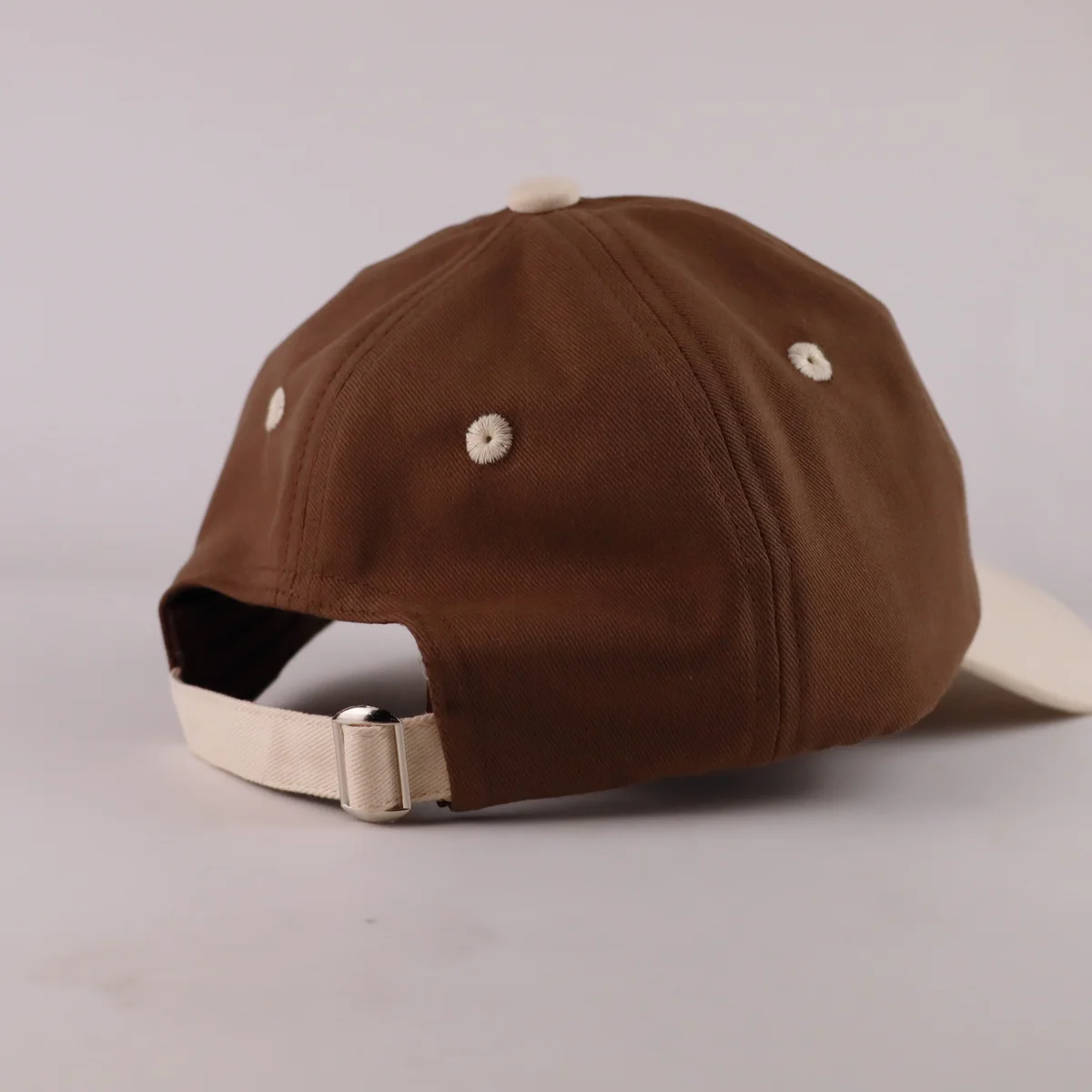 Rear of brown cap showing cream adjustable fabric strap with metal slider