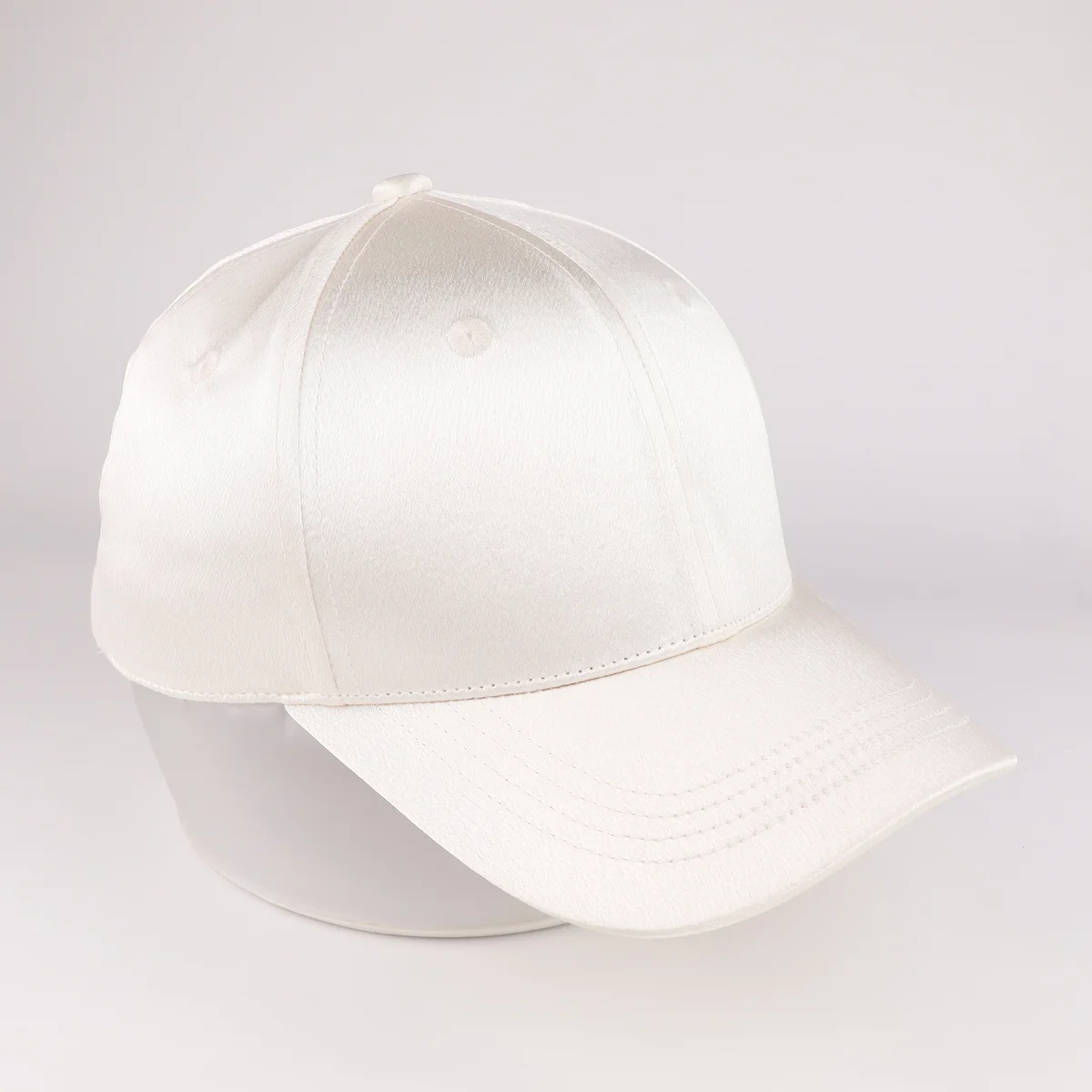 Three-quarter view showing subtle shine on ivory satin-look baseball cap