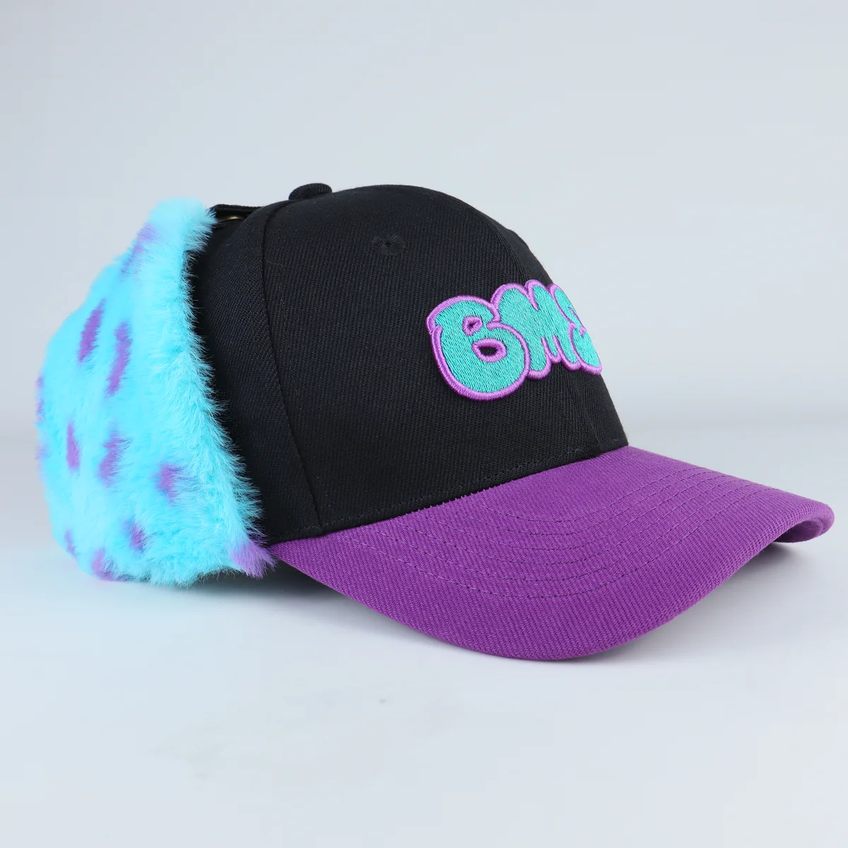 Front three-quarter view of novelty cap with purple visor turquoise fur panels and colorful front embroidery